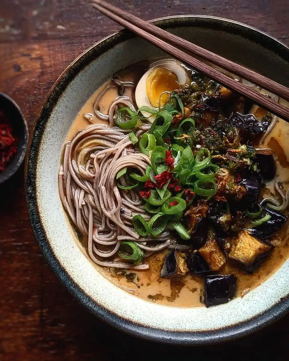 Bowl of tahini soba noodle soup topped with miso eggplant and fresh herbs