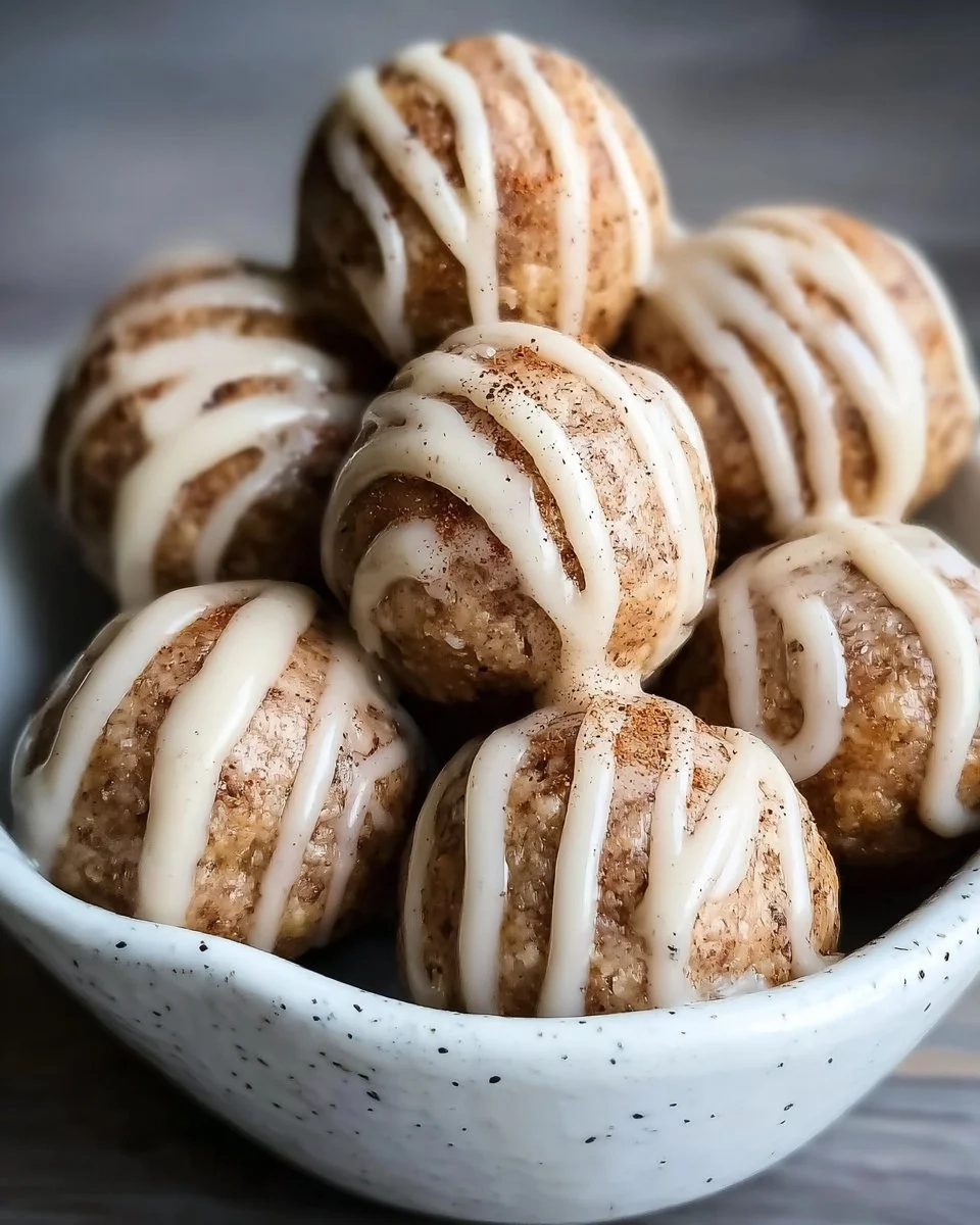 Cinnamon roll protein bites on a white plate with a sprinkle of cinnamon.