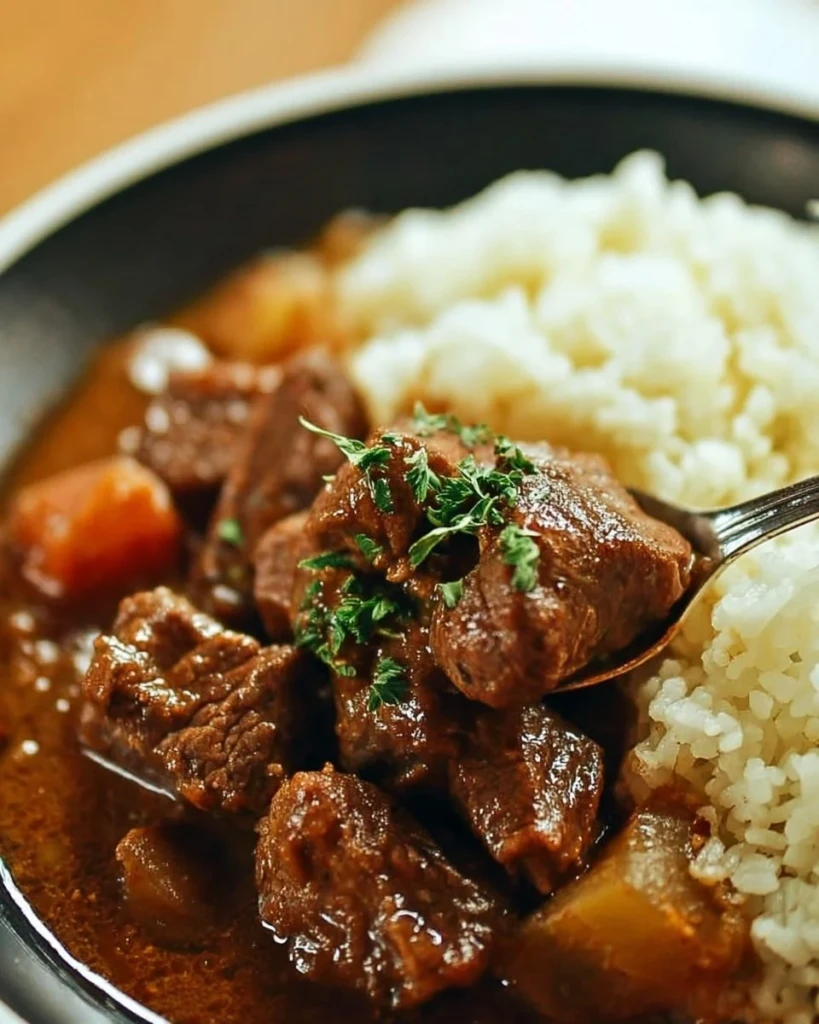 Delicious bowl of beef stew served with rice, garnished with fresh herbs.