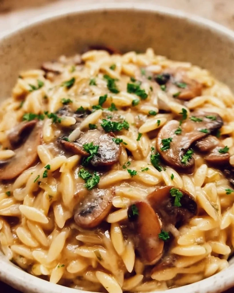 Plate of orzo with mushrooms, garnished with herbs and served in a bowl.